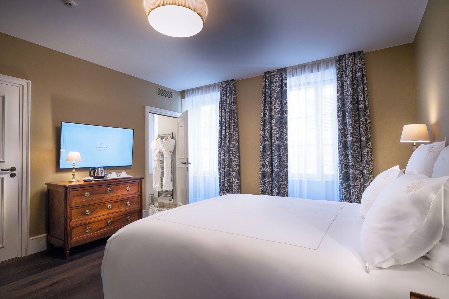 A hotel room with a large bed, a television on a wooden dresser, and a door leading to a bathroom.