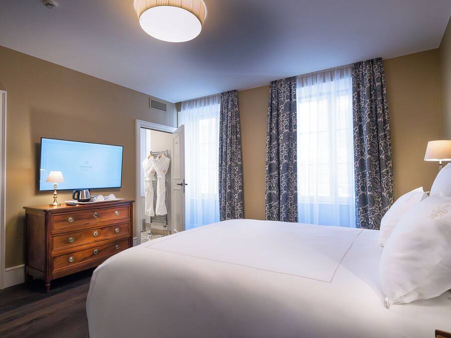 A hotel room with a large bed, a television on a wooden dresser, and a door leading to a bathroom.