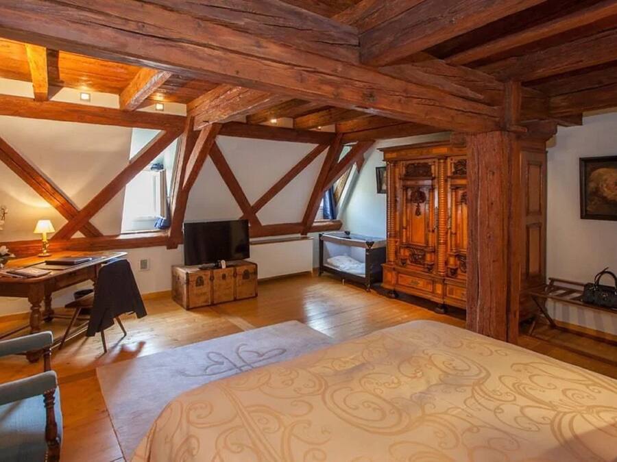 Una habitación rústica con vigas de madera a la vista, una cama con ropa de cama estampada, un escritorio con una lámpara y un armario de madera.