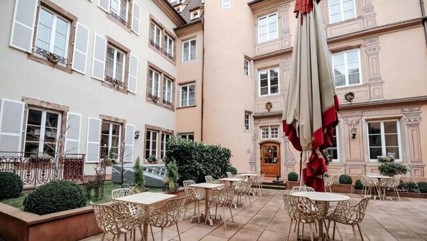 A courtyard with outdoor seating, a fountain, and a building with multiple windows and balconies. - Hotel & Spa Le Bouclier D'Or (Strasbourg)