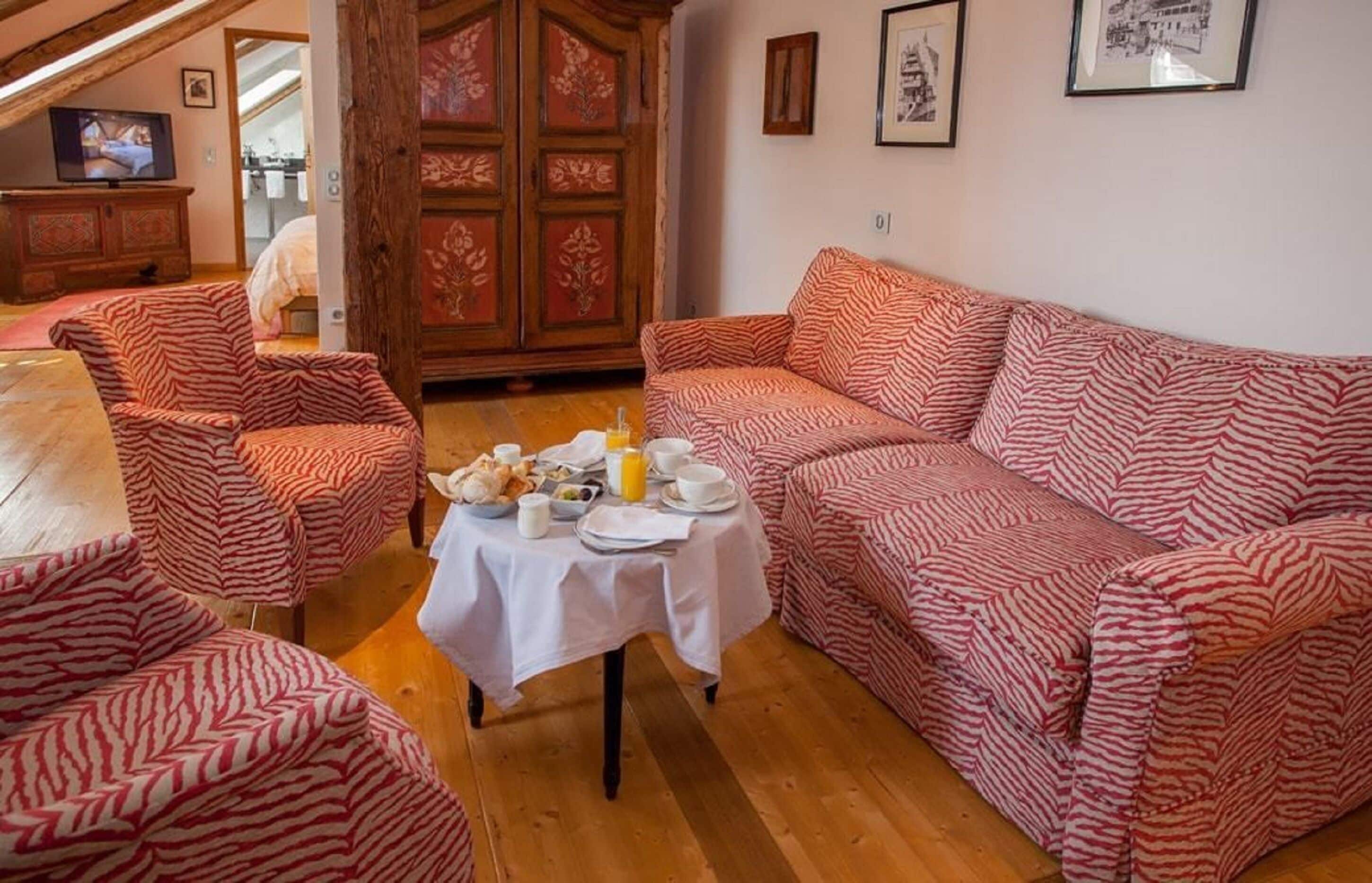 Uma sala de estar aconchegante com sofás estampados, uma mesa de jantar posta para o café da manhã e um armário de madeira.