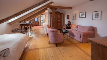 Ein gemütlicher Raum mit schrägen Wänden, Holzboden, einem Bett, einem Schlafsofa, einem Sessel, einem kleinen Tisch und einem Schrank.