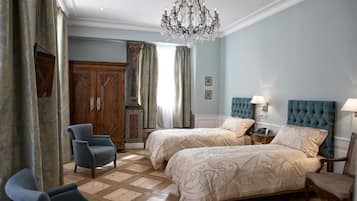 Una camera d'albergo con due letti, un lampadario, un armadio in legno, una sedia e un comodino.