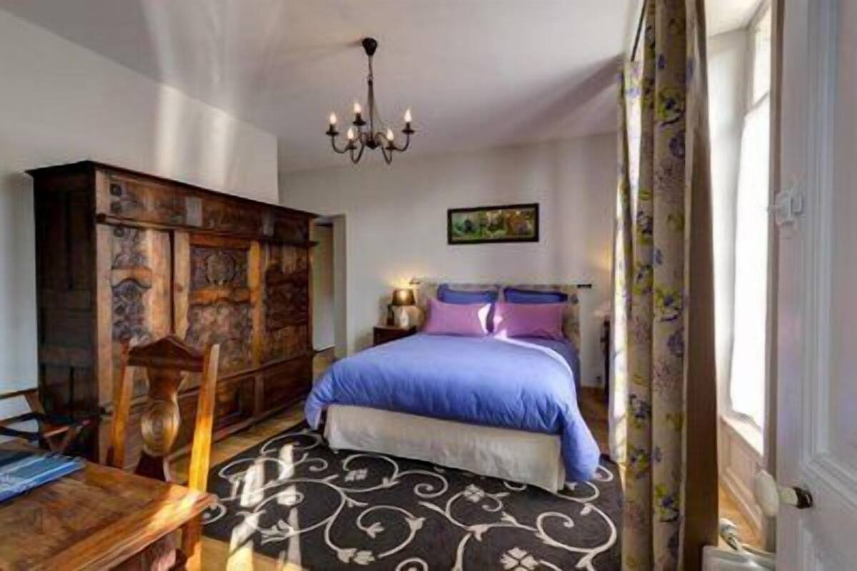 Quarto com cama, guarda-roupa de madeira, lustre e janela com cortinas.