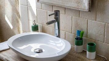 A white sink with a modern faucet, a green soap dispenser, and two green and white toothbrush holders on a beige countertop.