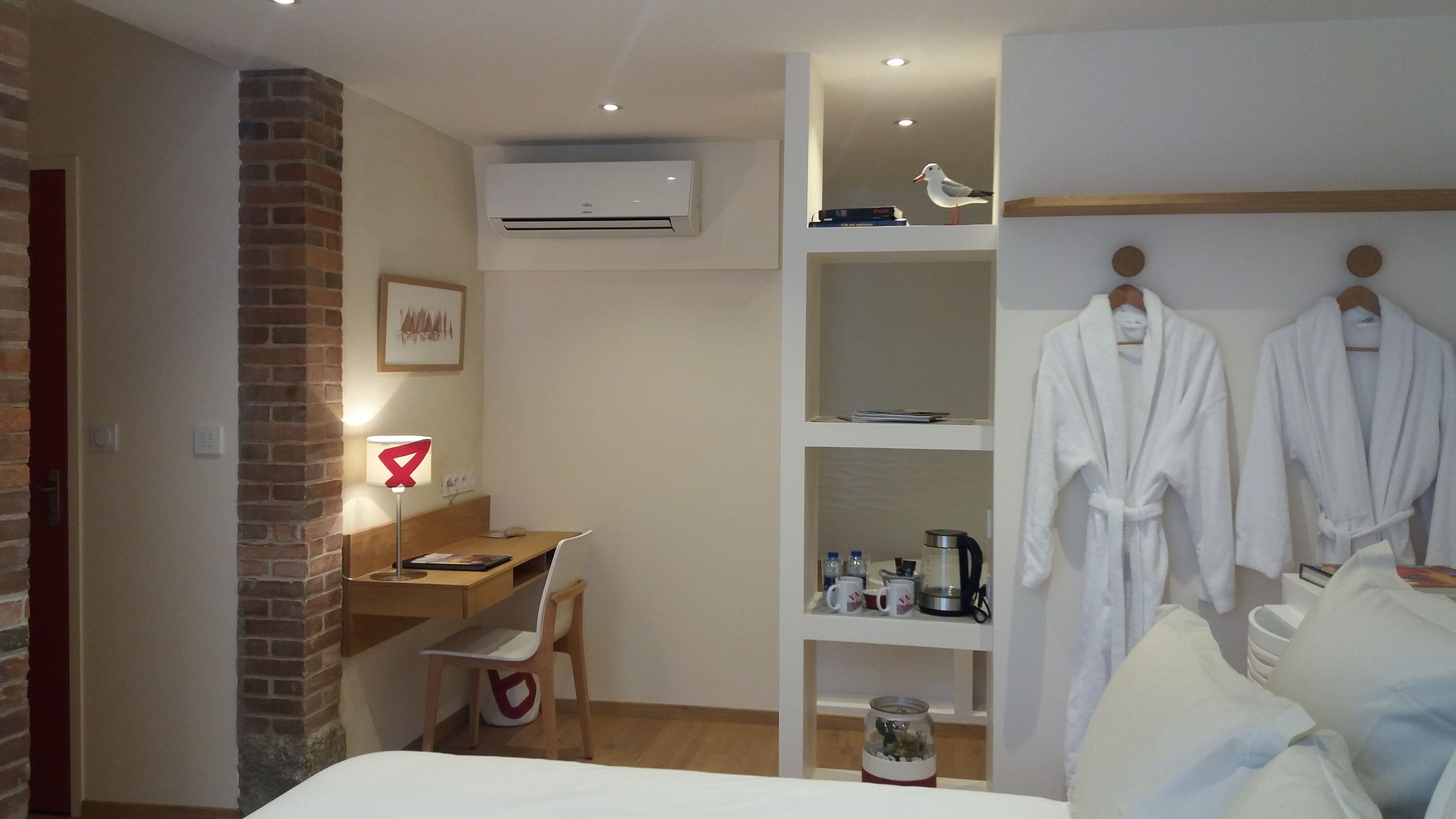 Ein Hotelzimmer mit einem Bett, einem Schreibtisch, einem Stuhl, einem Bücherregal und zwei weißen Bademänteln, die auf einem Gestell hängen.