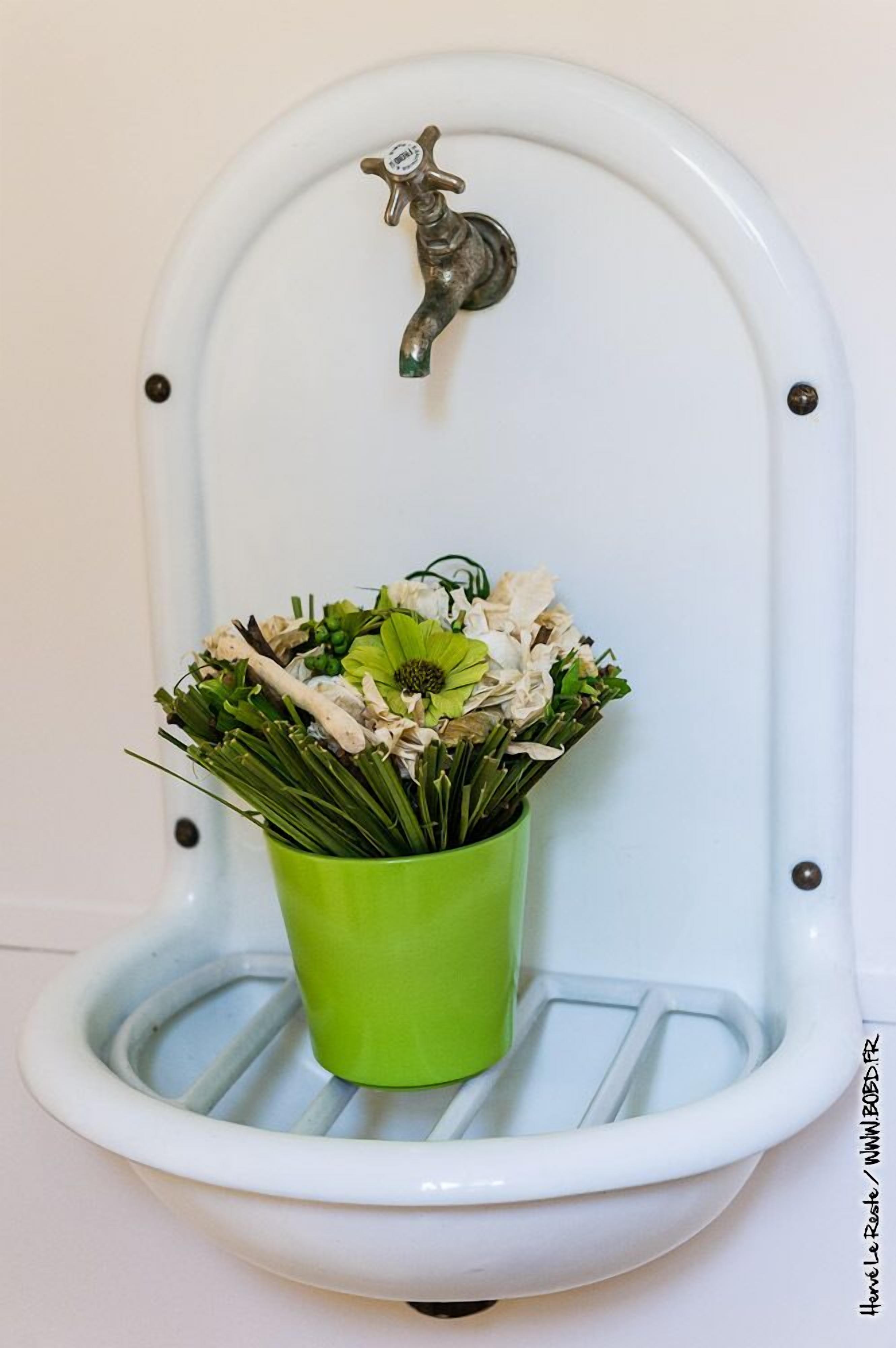 Un inodoro con un cubo verde lleno de flores.