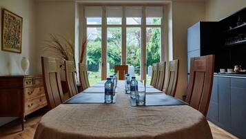 A dining table set with water bottles and glasses, flanked by wooden chairs, in a room with a large window and a chandelier.