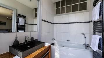 Un baño moderno con un lavabo negro, tocador de madera, un espejo grande y una bañera blanca.
