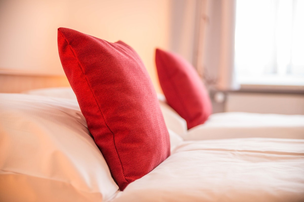 Una cama con ropa de cama blanca y dos almohadas rojas.