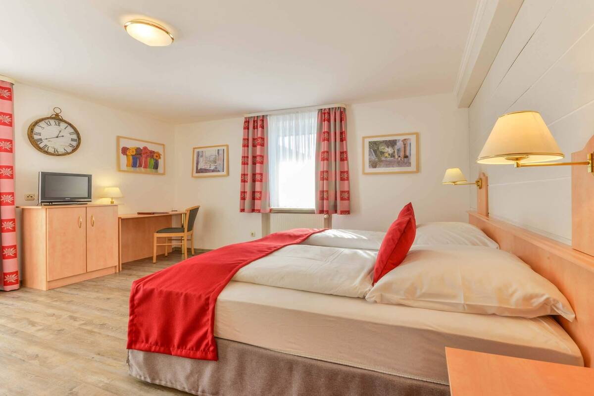 Una habitación de hotel con una cama, un escritorio, un televisor y un reloj en la pared.