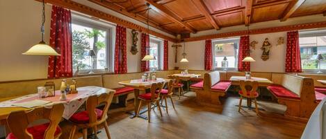Un restaurant avec des tables et des bancs en bois, des rideaux rouges et des lampes suspendues.