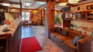 A cozy interior with a wooden reception desk, a leather sofa, and a red carpet leading to the bar area. - Landhotel & Brauhaus Prignitzer Hof (Pritzwalk)