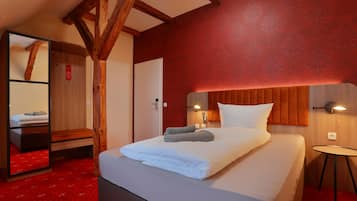 Une chambre d’hôtel avec un lit, une tête de lit en bois, un mur à motifs rouges et une petite table avec une lampe.