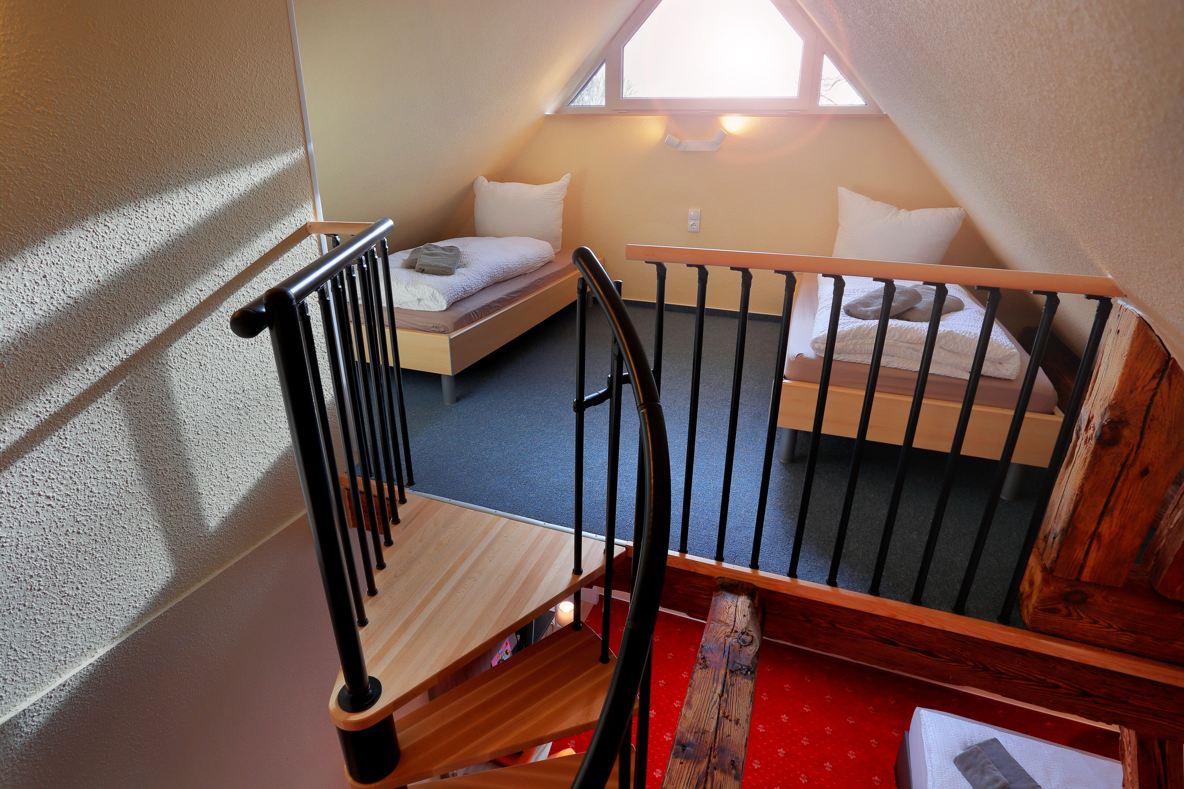 Une chambre de type dortoir avec deux lits simples, un escalier en bois et une moquette rouge.