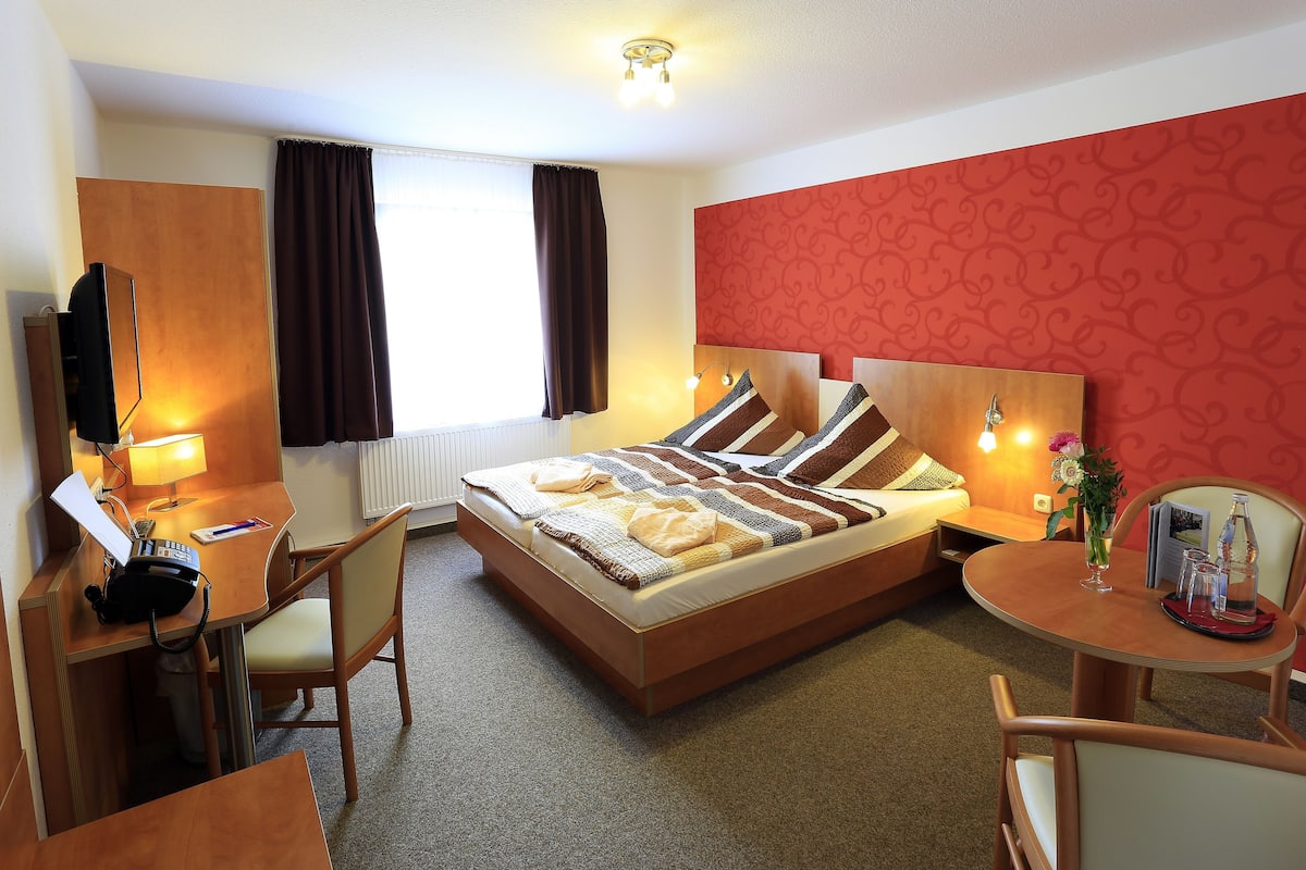 A hotel room with a bed, desk, chair, and a small table with a tray.