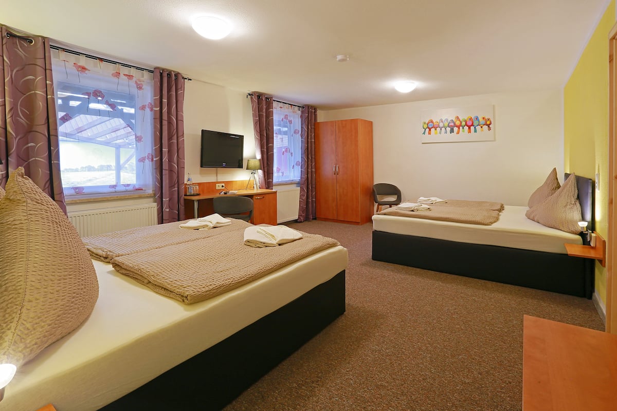 A hotel room with two beds, a desk, a chair, a television, and a window with curtains.