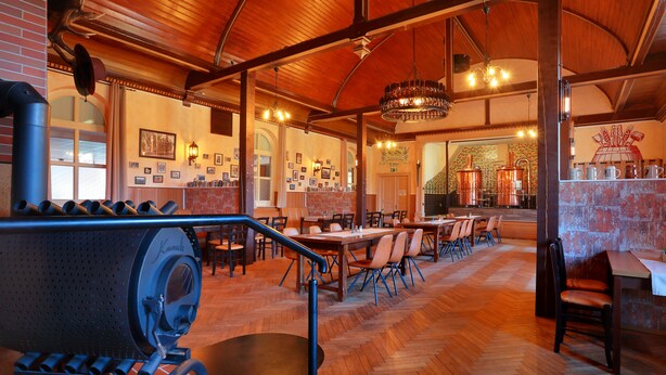 A restaurant with wooden floors, tables, chairs, and a bar area with a large beer keg. - Landhotel & Brauhaus Prignitzer Hof (Pritzwalk)