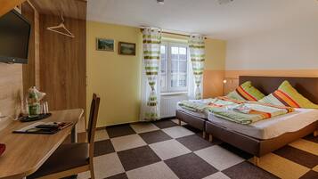 A room with a checkered floor, a bed with colorful pillows, a desk with a lamp, and a TV mounted on the wall.