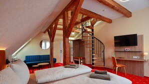 A modern hotel room with a large bed, a blue sofa, a small table, a TV, and a wooden staircase. - Landhotel & Brauhaus Prignitzer Hof (Pritzwalk)