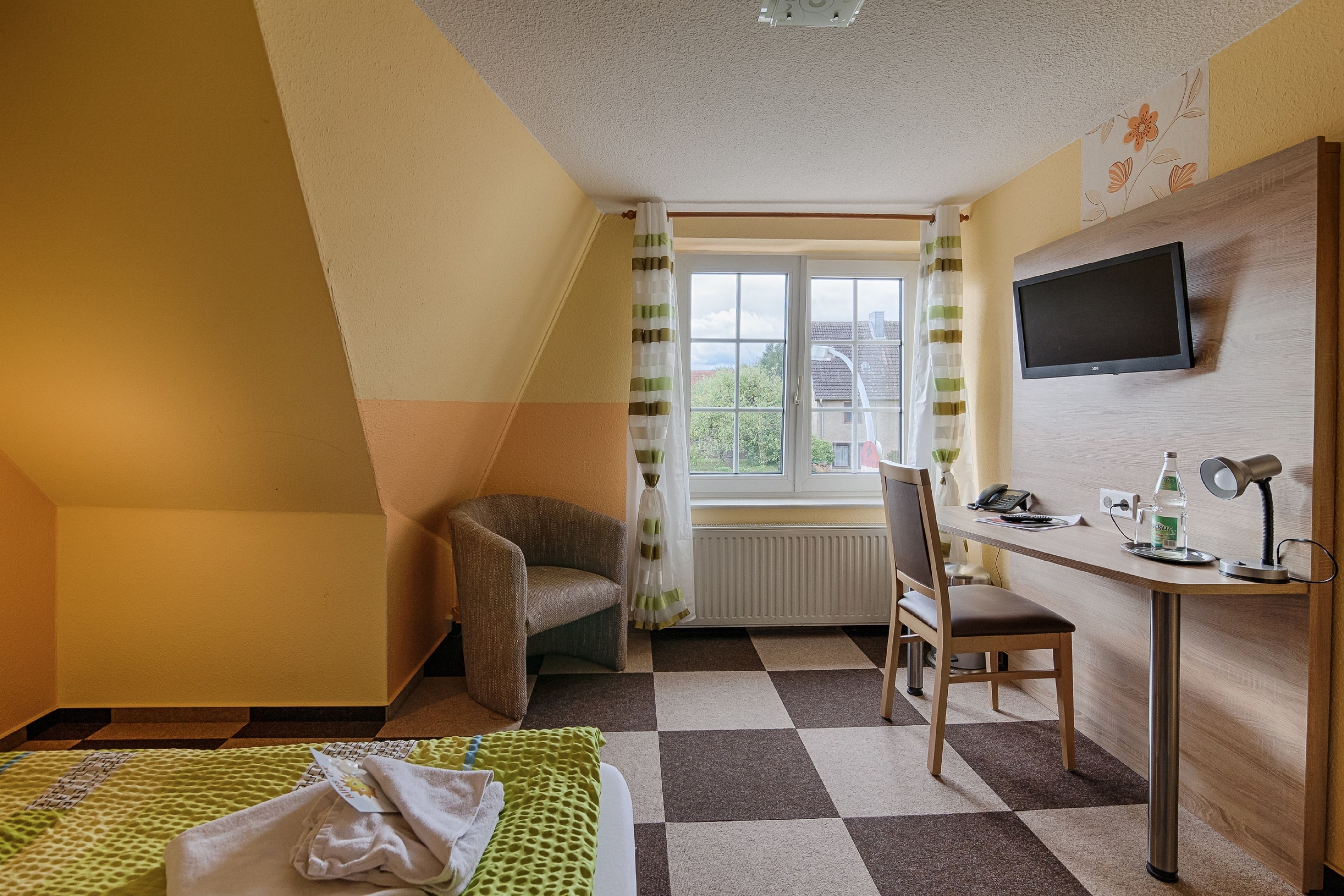 A room with a bed, a desk, a chair, a television, and a window with curtains.