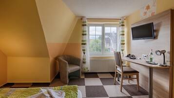 A room with a bed, a desk, a chair, a television, and a window with curtains.