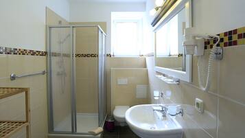 Baño con cabina de ducha de vidrio, inodoro y lavamanos con espejo.