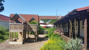 A courtyard with a wooden play structure, a garden with yellow flowers, and traditional buildings with red-tiled roofs. - Landhotel & Brauhaus Prignitzer Hof (Pritzwalk)