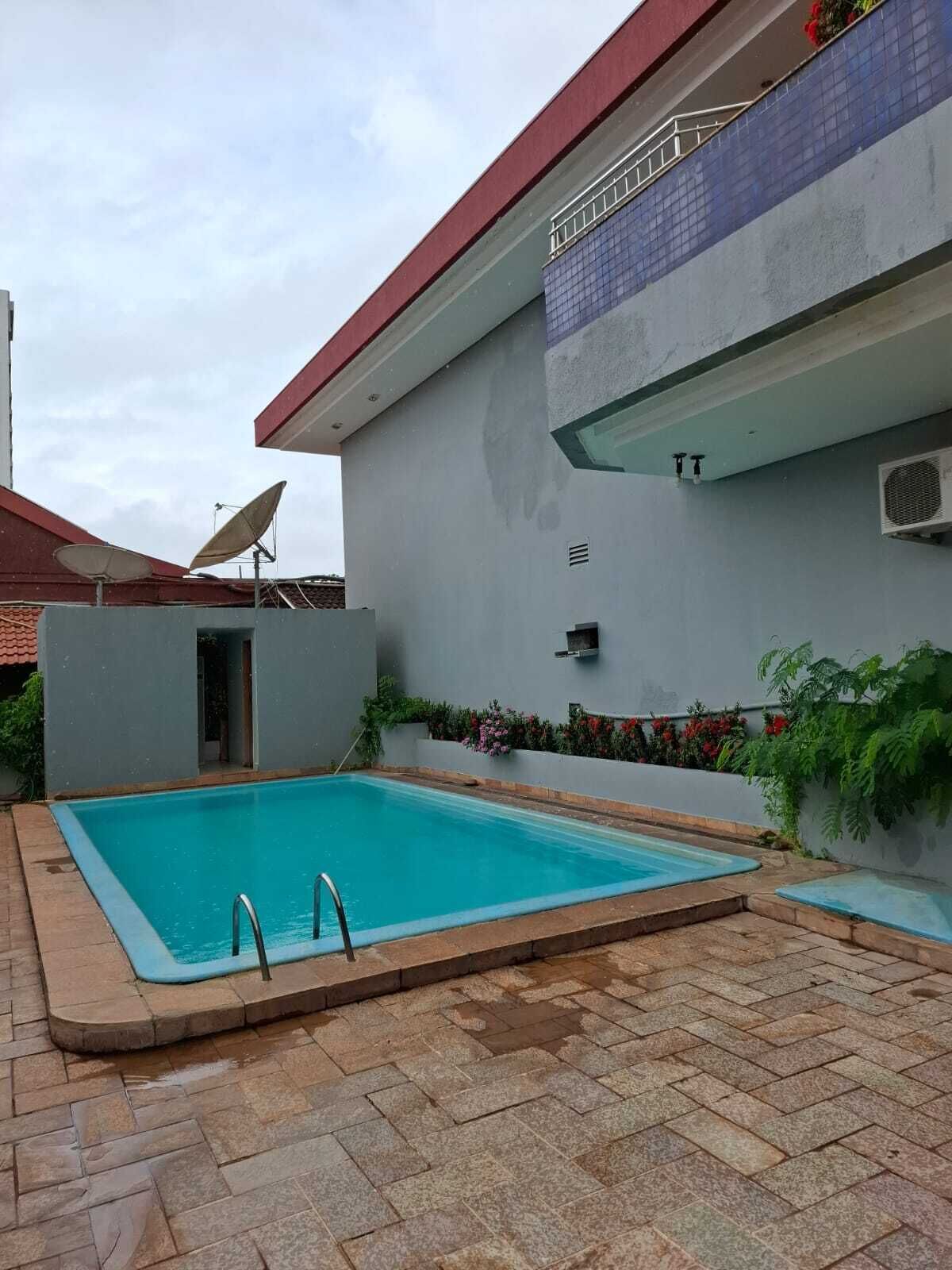A swimming pool with a tiled deck, a satellite dish, and a small garden area with flowers.