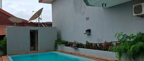 A swimming pool with a tiled deck, a satellite dish, and a small garden area with flowers.
