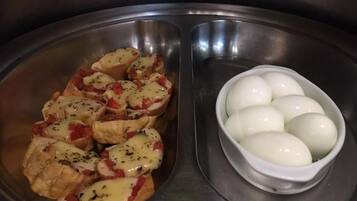 En rustfri stålvask med en skål kogte æg og et fad mad, sandsynligvis kylling eller fisk, toppet med ost og krydderurter.