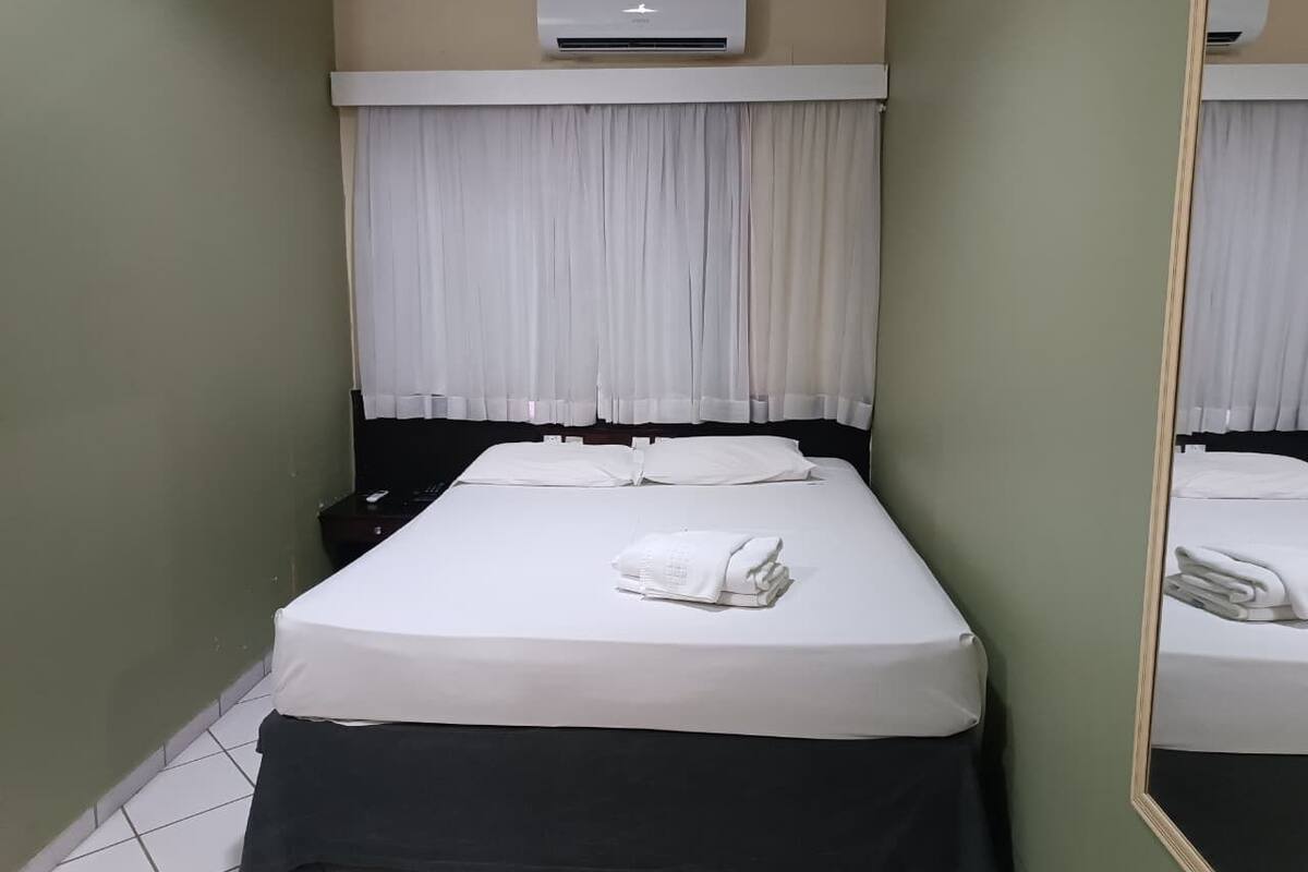 Une chambre d’hôtel comprenant un lit, une table de chevet, un appareil de climatisation et un miroir.