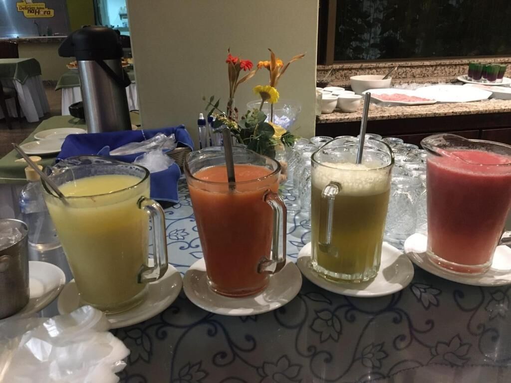 Una mesa de buffet con diversas bebidas, entre ellas zumos y batidos, y una máquina de café al fondo.
