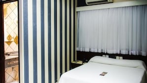 Hotellihuone, jossa on sänky, yöpöytä, ikkuna verhoilla ja seinä, jossa on pystysuorat raidat.