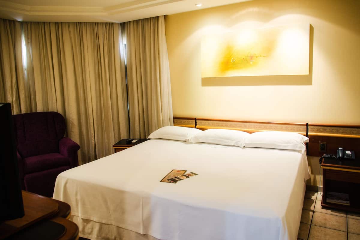 Une chambre d’hôtel avec un grand lit, une chaise, un bureau avec un téléphone et un luminaire fixé au mur.