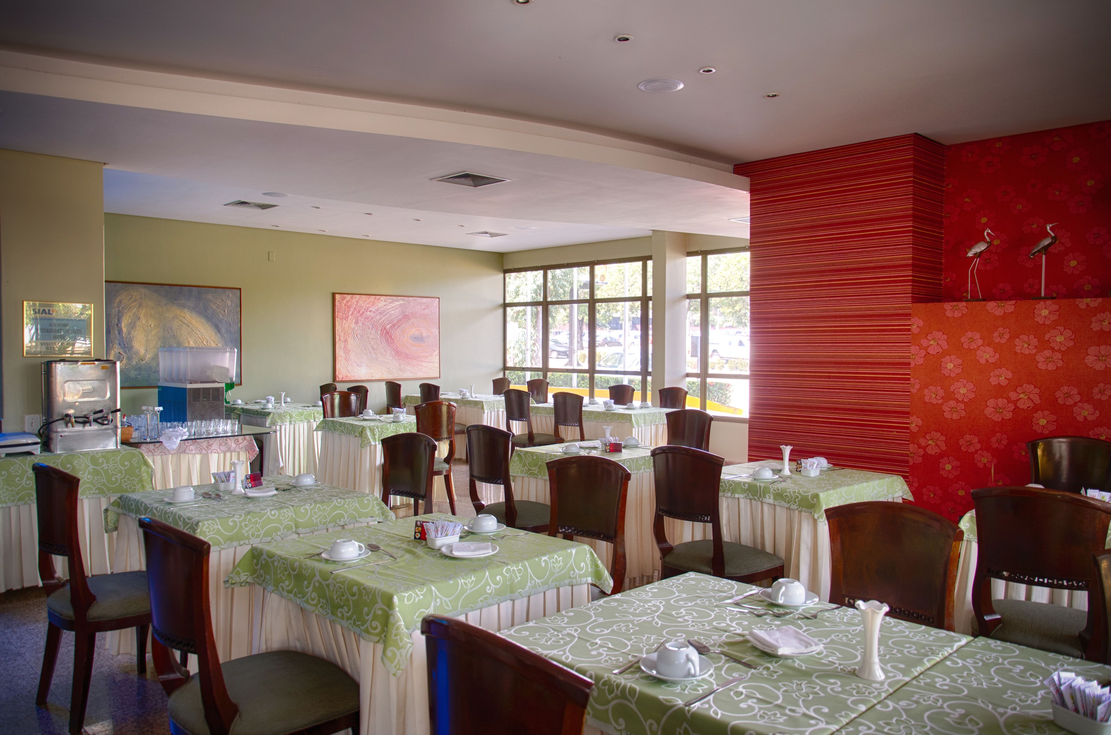 Un comedor con varias mesas y sillas, ventanas amplias y obras de arte en las paredes.