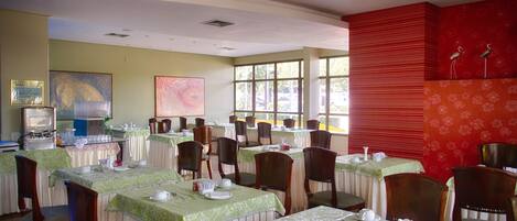 Un comedor con varias mesas y sillas, ventanas amplias y obras de arte en las paredes.