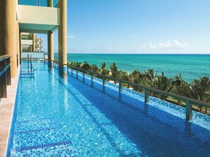 Ein langer, klarer blauer Pool mit Fliesenrand, der auf einen Strand und das Meer hinausblickt.