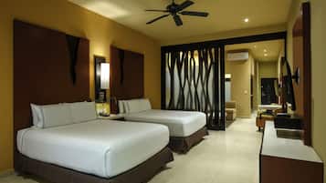 A hotel room with two beds, a desk, a chair, a TV, and a ceiling fan.