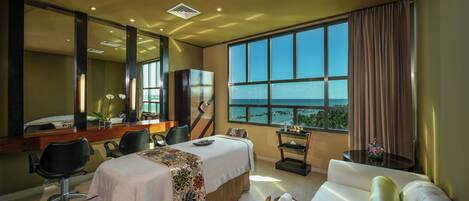 Habitación de hotel con cama, sofá, escritorio con silla, ventana grande y espejo.