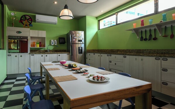 Ein Restaurant mit Schachbrettboden, einem langen Tisch mit verschiedenen Speisen und einer grünen Wand mit hängenden Küchenutensilien.