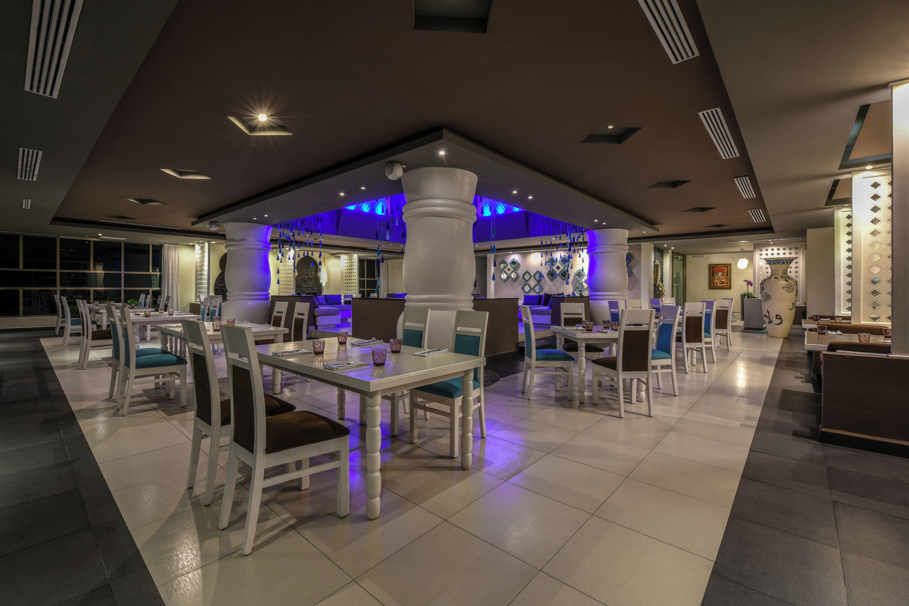 A modern restaurant with white tables and chairs, blue cushions, and a central column.