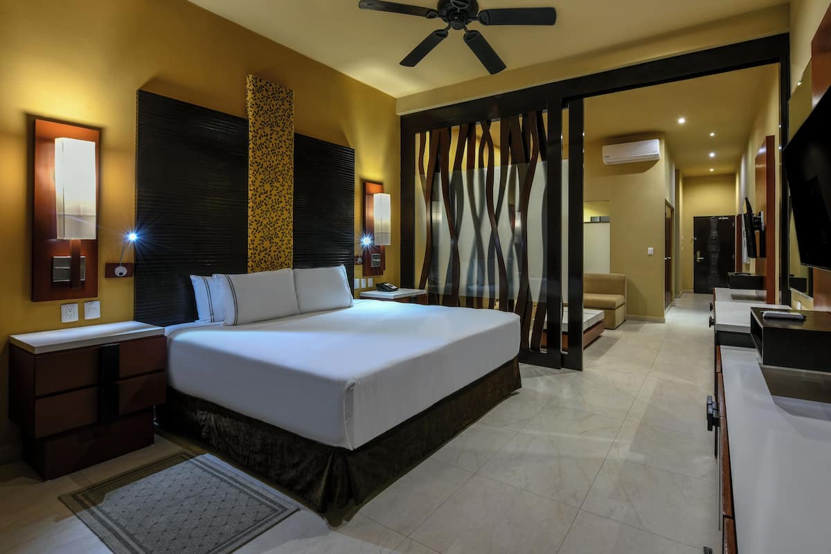 A modern hotel room with a large bed, bedside tables, a desk, a TV, and an air conditioning unit.