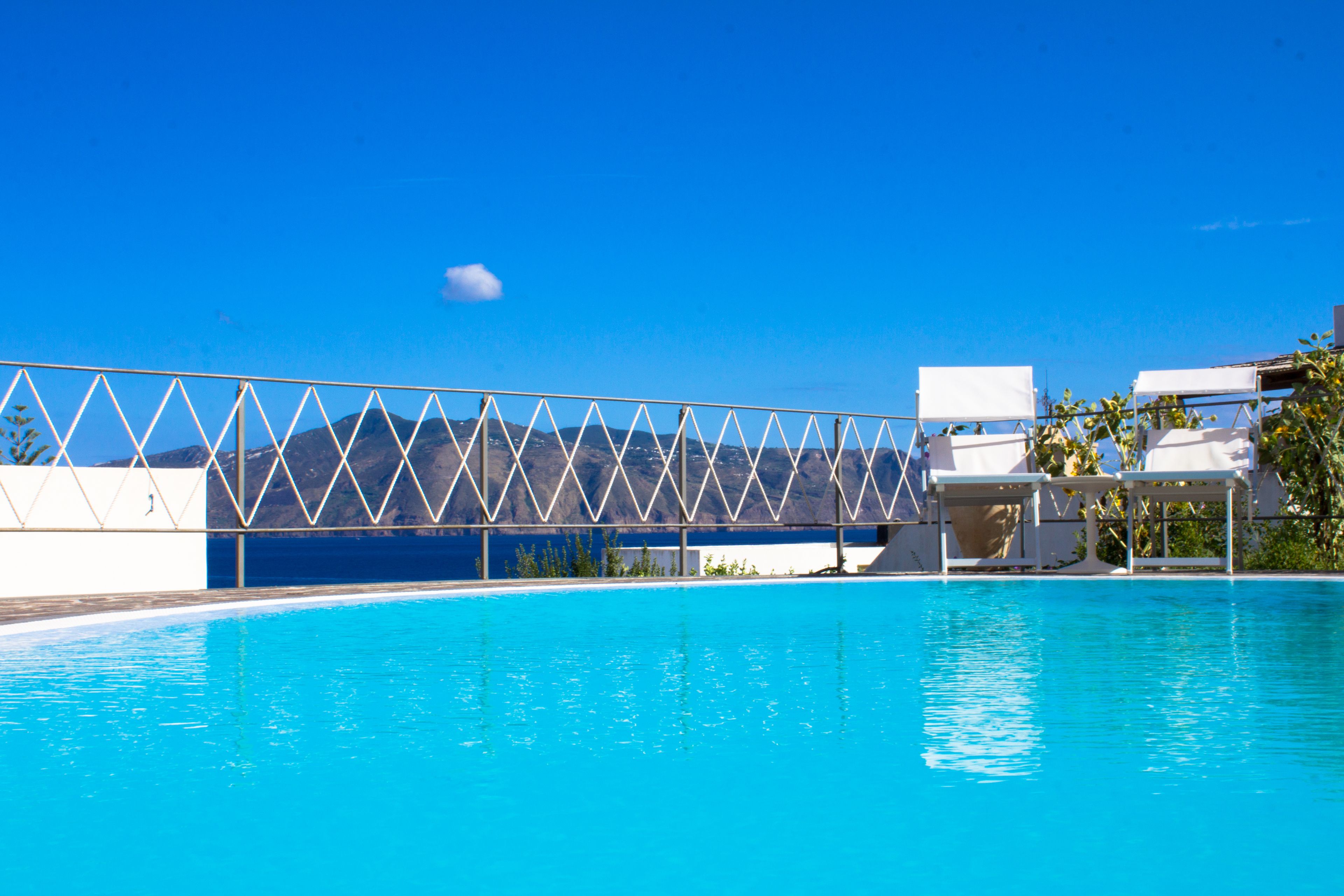 A clear blue pool with a metal fence and lounge chairs.