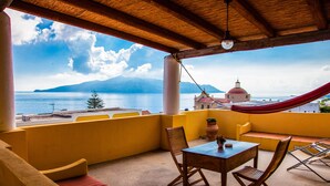 A balcony with yellow walls, a wooden table, and two wooden chairs. A red hammock is draped over the railing. - Hotel Arcangelo - Salina (Santa Marina Salina)