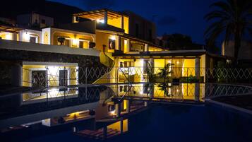 A modern hotel with a swimming pool, multiple balconies, and a well-lit exterior at night.