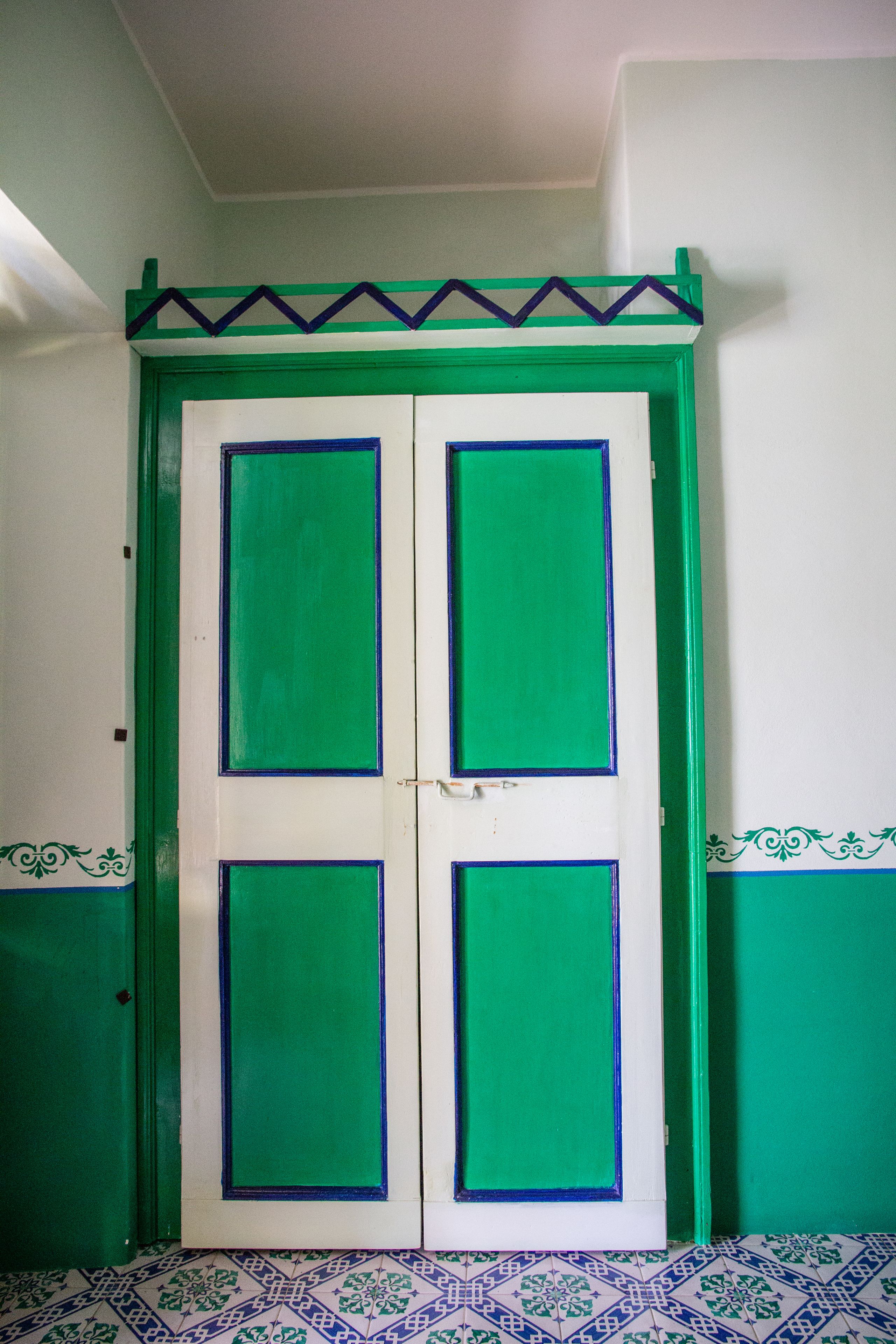 A room with a green and white door, patterned floor tiles, and a decorative border on the walls.
