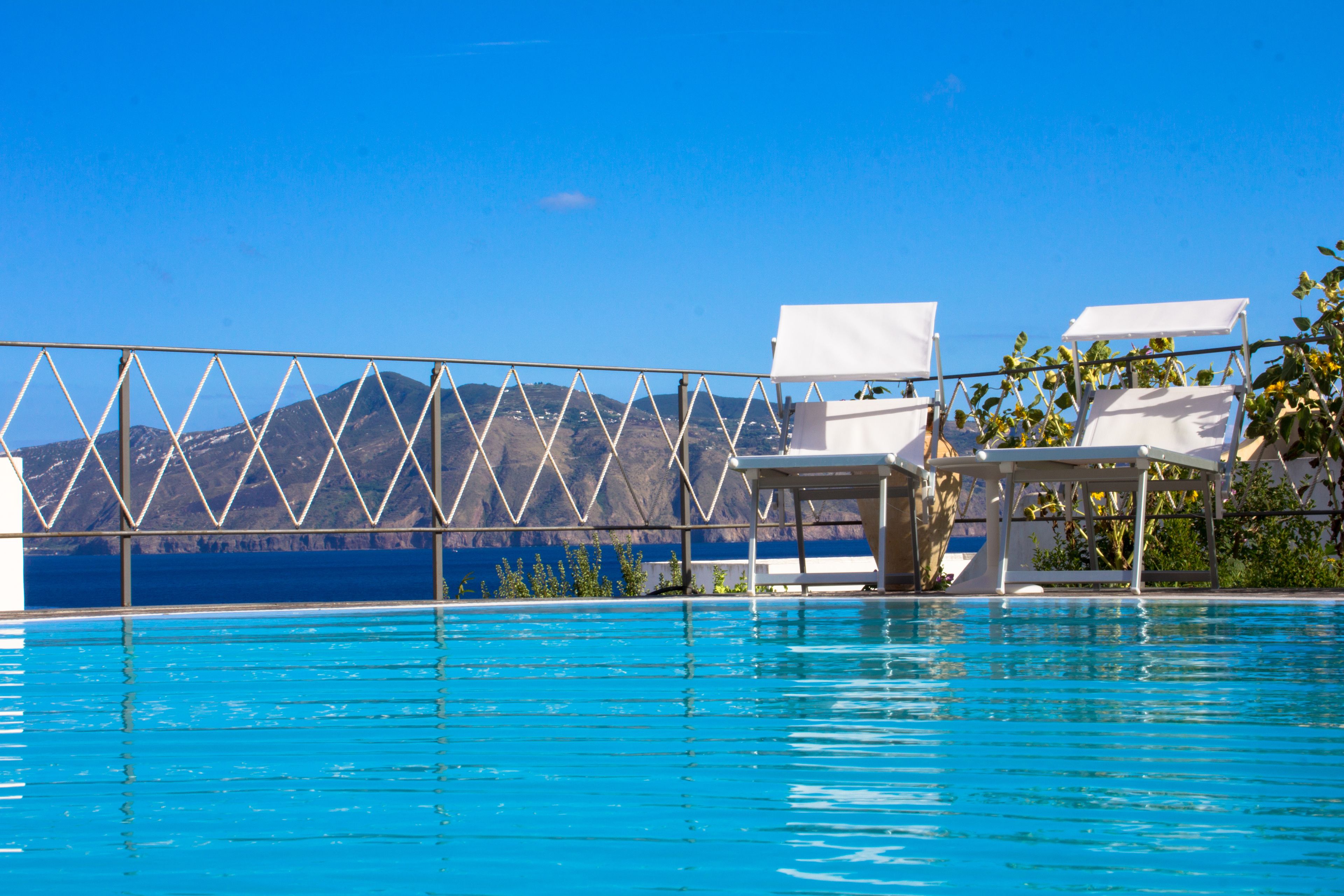 A swimming pool with white lounge chairs and a view of mountains in the background.