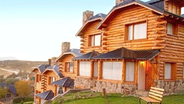 Una hilera de cabañas de madera con cimientos de piedra, contraventanas de madera y un césped.