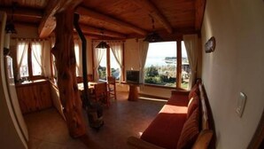 Un interior de madera acogedor con sofá, televisor y comedor, con vistas a un paisaje idílico.